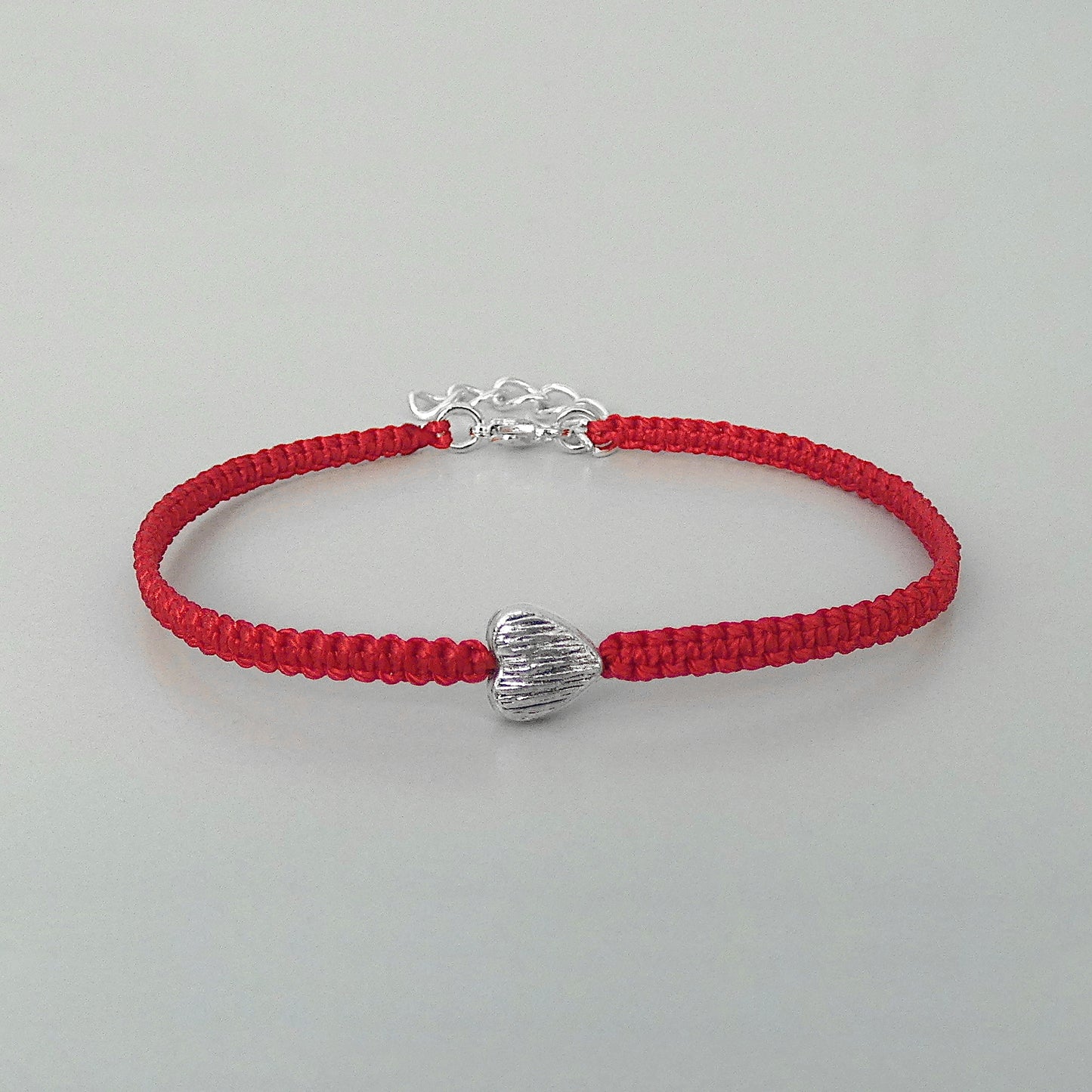 Red seven inch macramé bracelet with silver plated textured heart charm, lobster clasp and one inch extender chain.