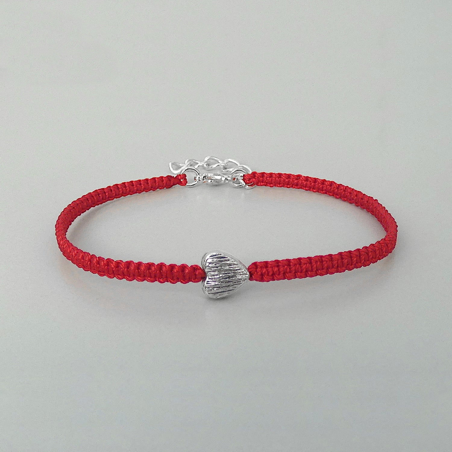 Red seven inch macramé bracelet with silver plated textured heart charm, lobster clasp and one inch extender chain.