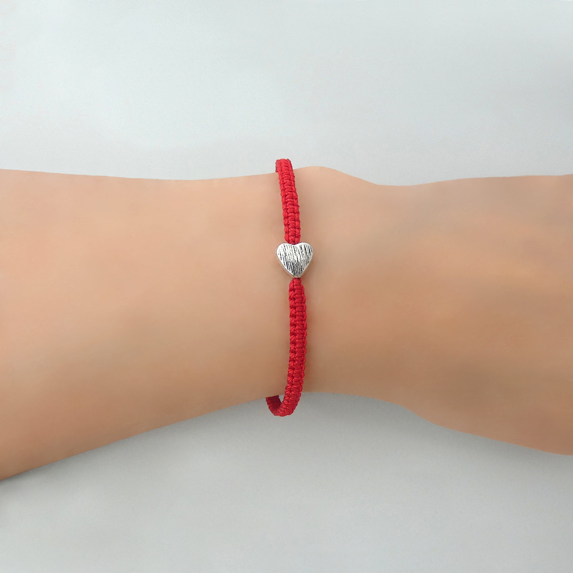 Red seven inch macramé bracelet with silver plated textured heart charm, lobster clasp and one inch extender chain on a woman's wrist.