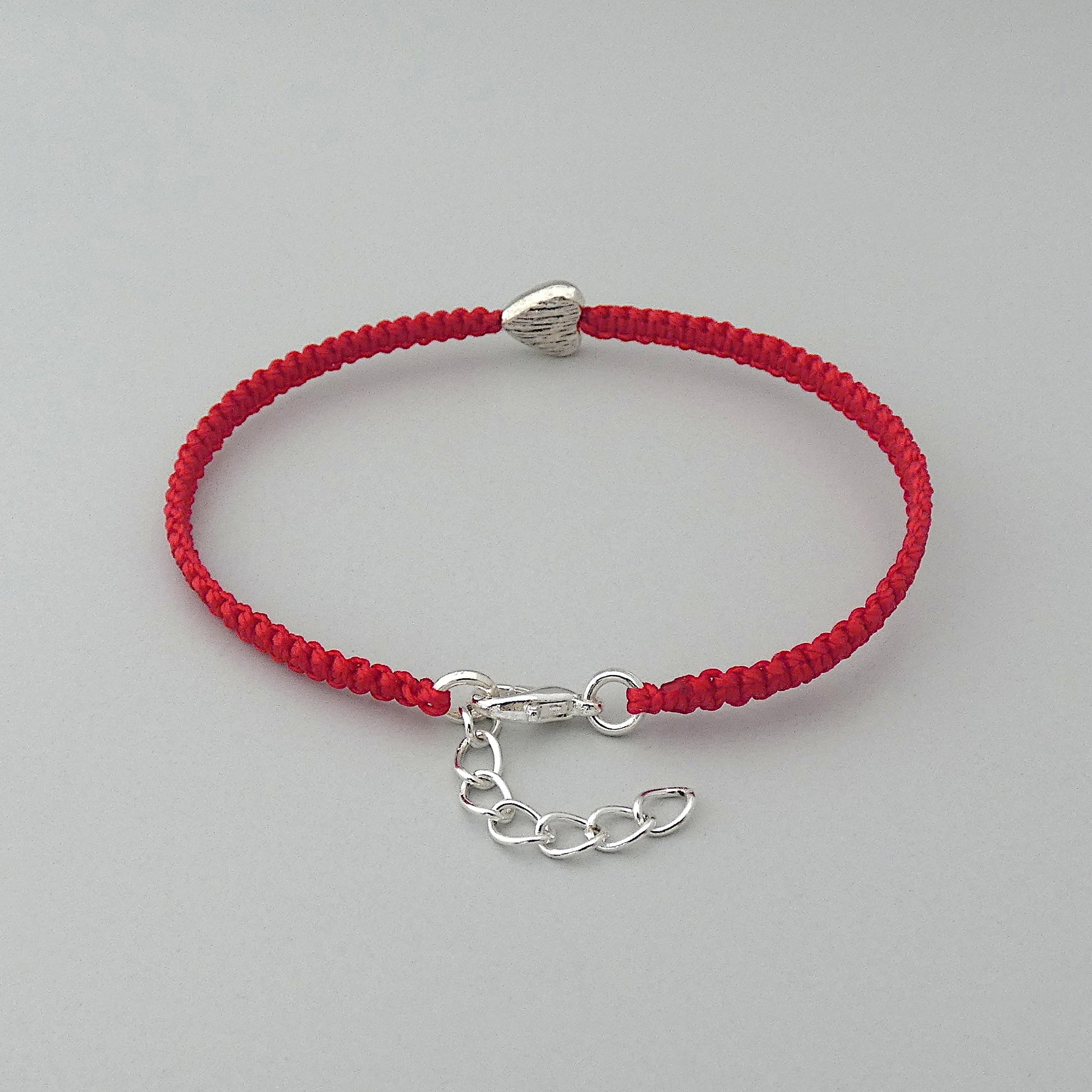 Silver plated lobster claw clasp and one inch extender chain on a red seven inch macramé bracelet with silver plated textured heart charm.