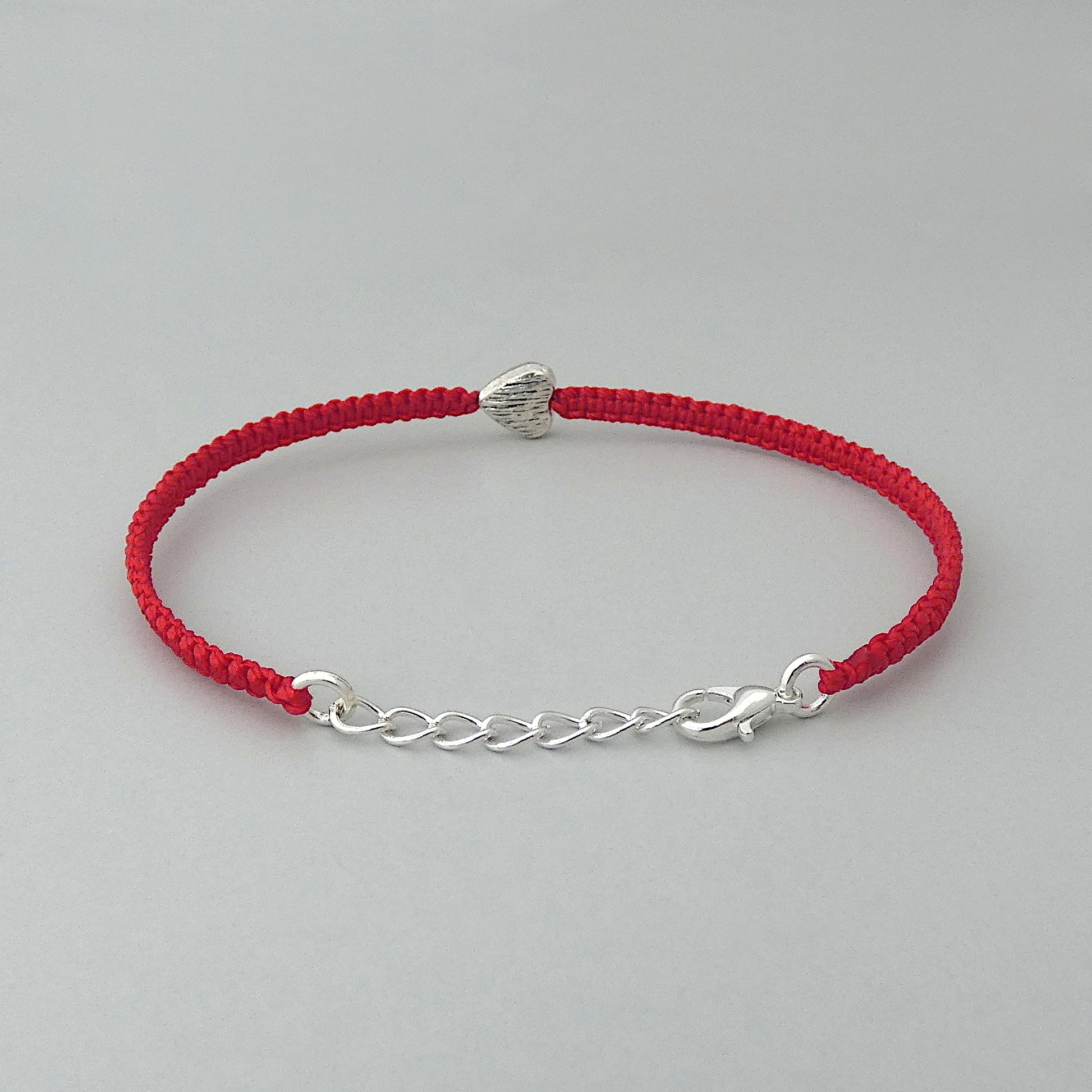 Silver plated lobster claw clasp attached to a one inch extender chain on a red seven inch macramé bracelet with silver plated textured heart charm.