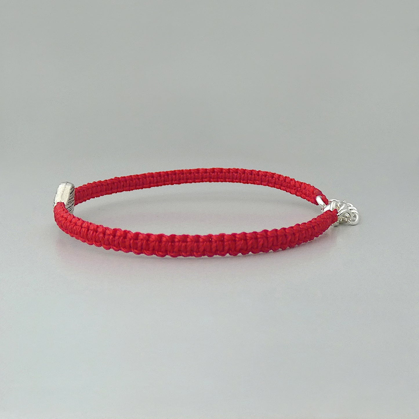 Side view of the knots on a red seven inch macramé bracelet with silver plated textured heart charm.