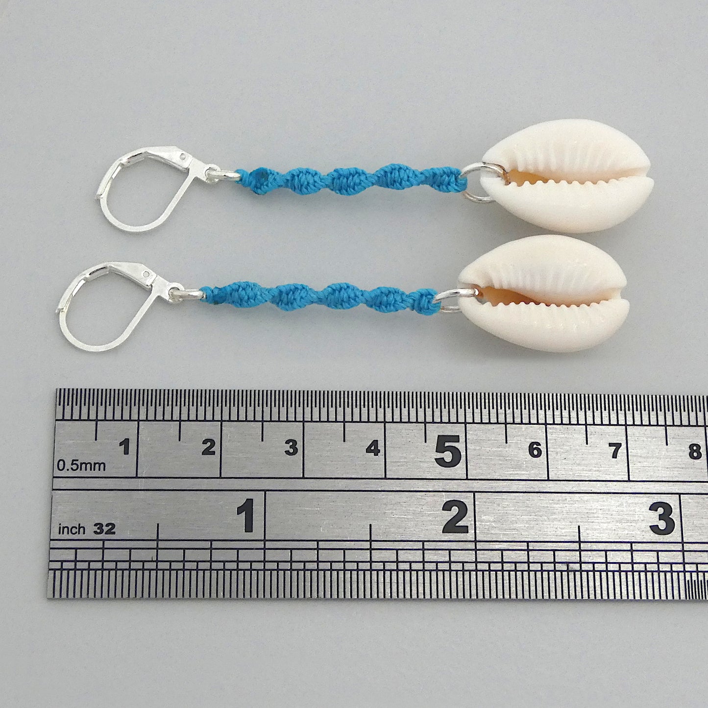 Silver plated leverback earrings with cowrie shells and blue macramé twist detail.