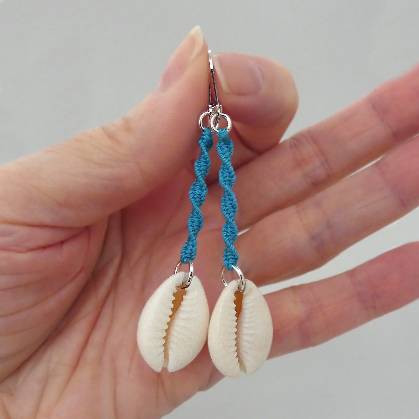 Silver plated leverback earrings with cowrie shells and blue macramé twist detail.