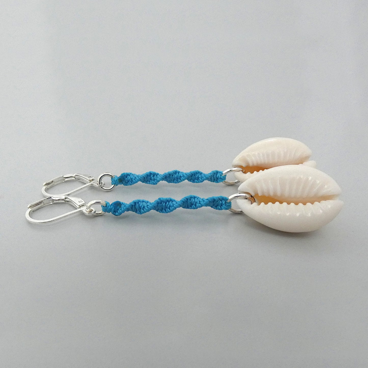 Silver plated leverback earrings with cowrie shells and blue macramé twist detail.