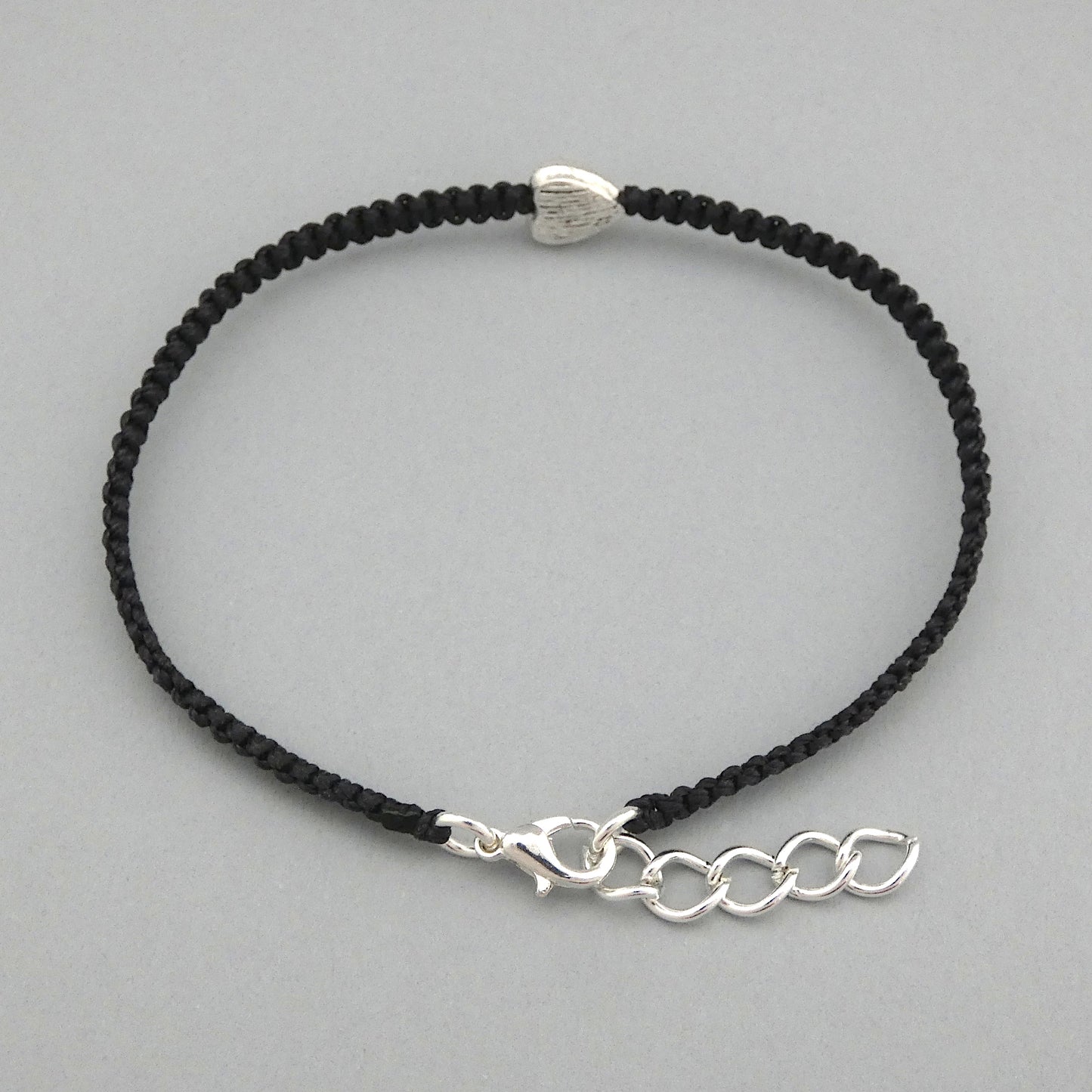 Close up of the lobster claw clasp and extender chain on a black seven inch macramé bracelet with silver plated textured heart charm, lobster clasp and one inch extender chain.