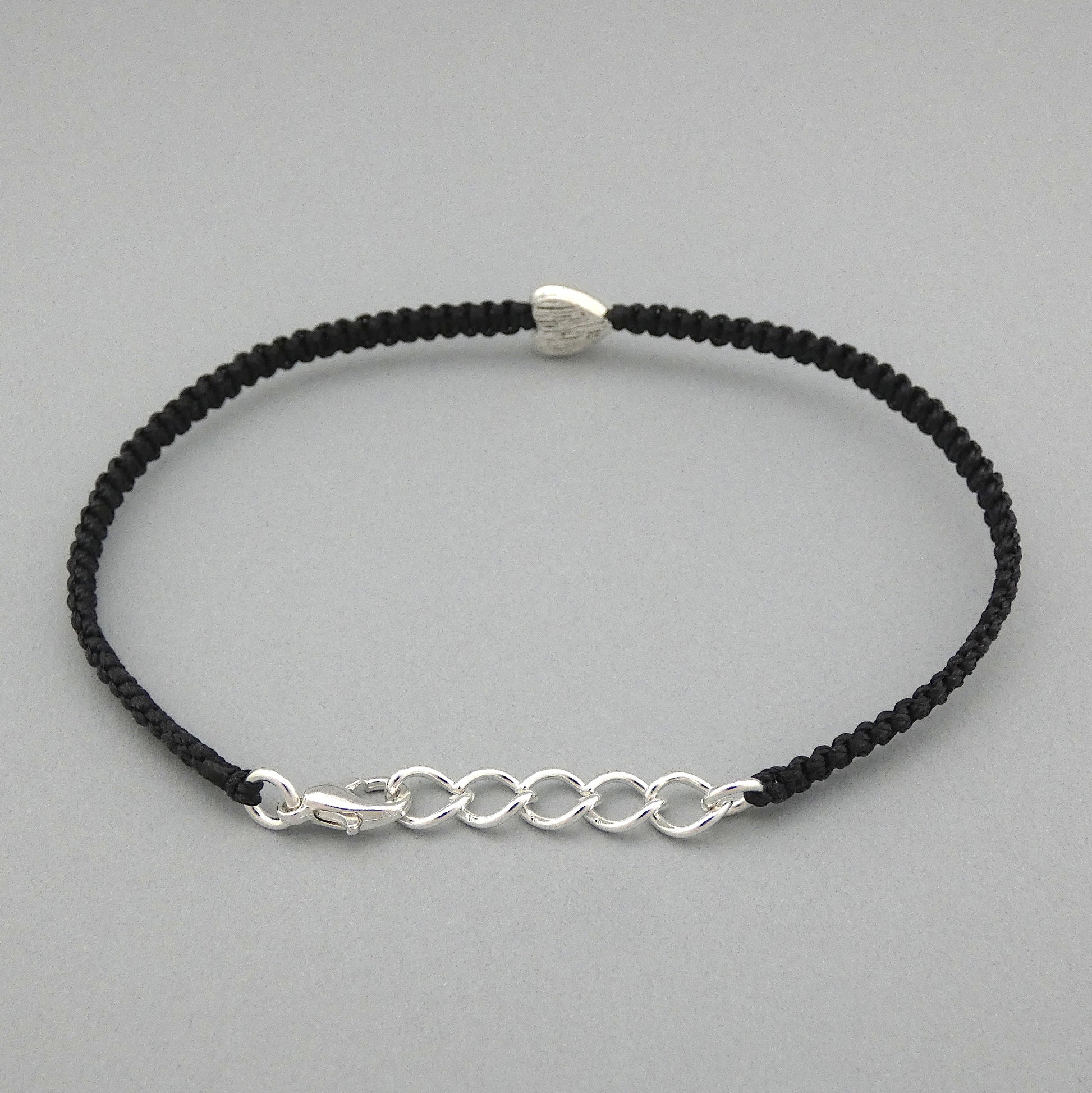 Black seven inch macramé bracelet with silver plated textured heart charm, lobster clasp and one inch extender chain. The bracelet is fully extended to eight inches.