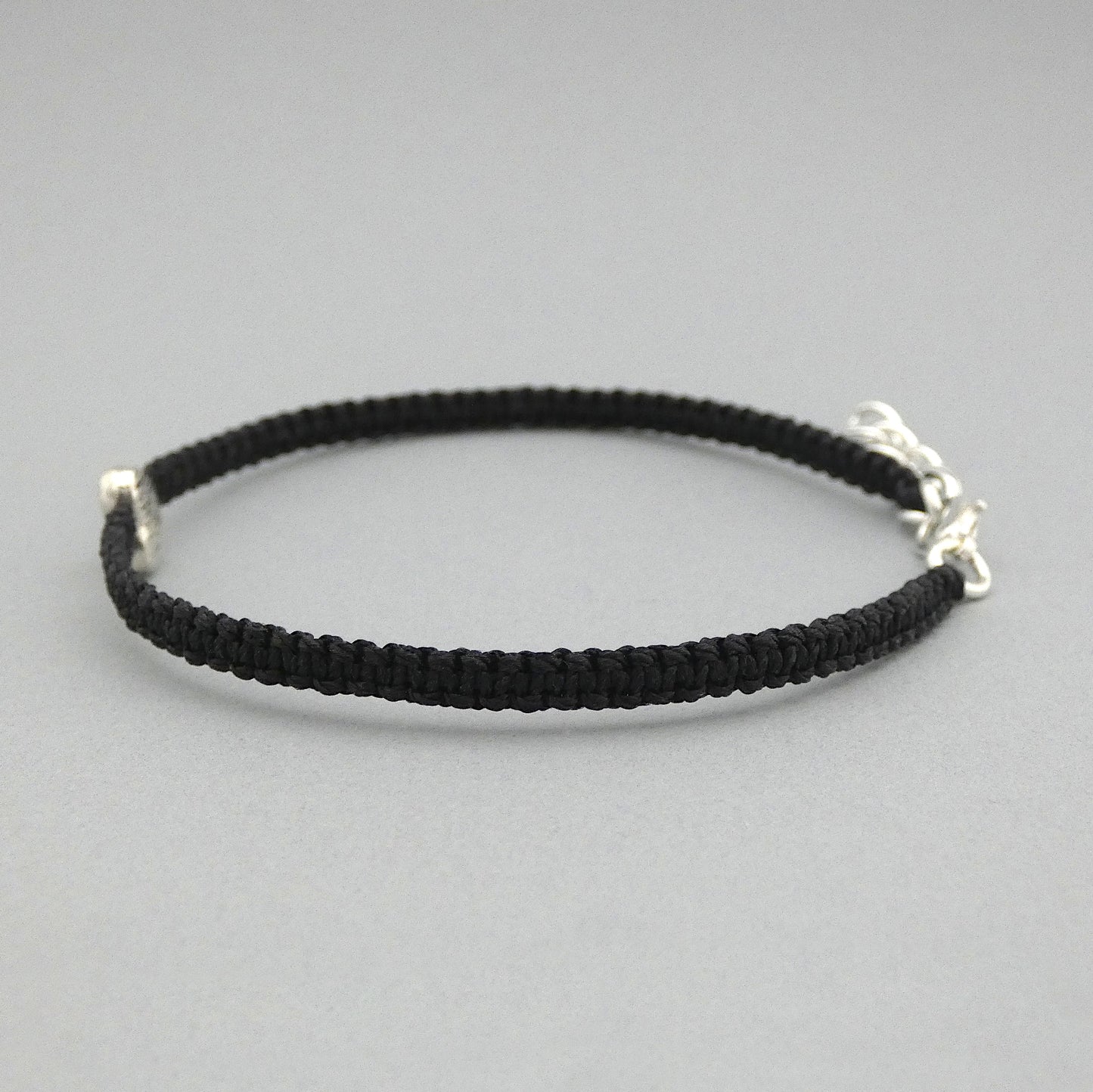 Side view of the knots on a black seven inch macramé bracelet with silver plated textured heart charm, lobster clasp and one inch extender chain.