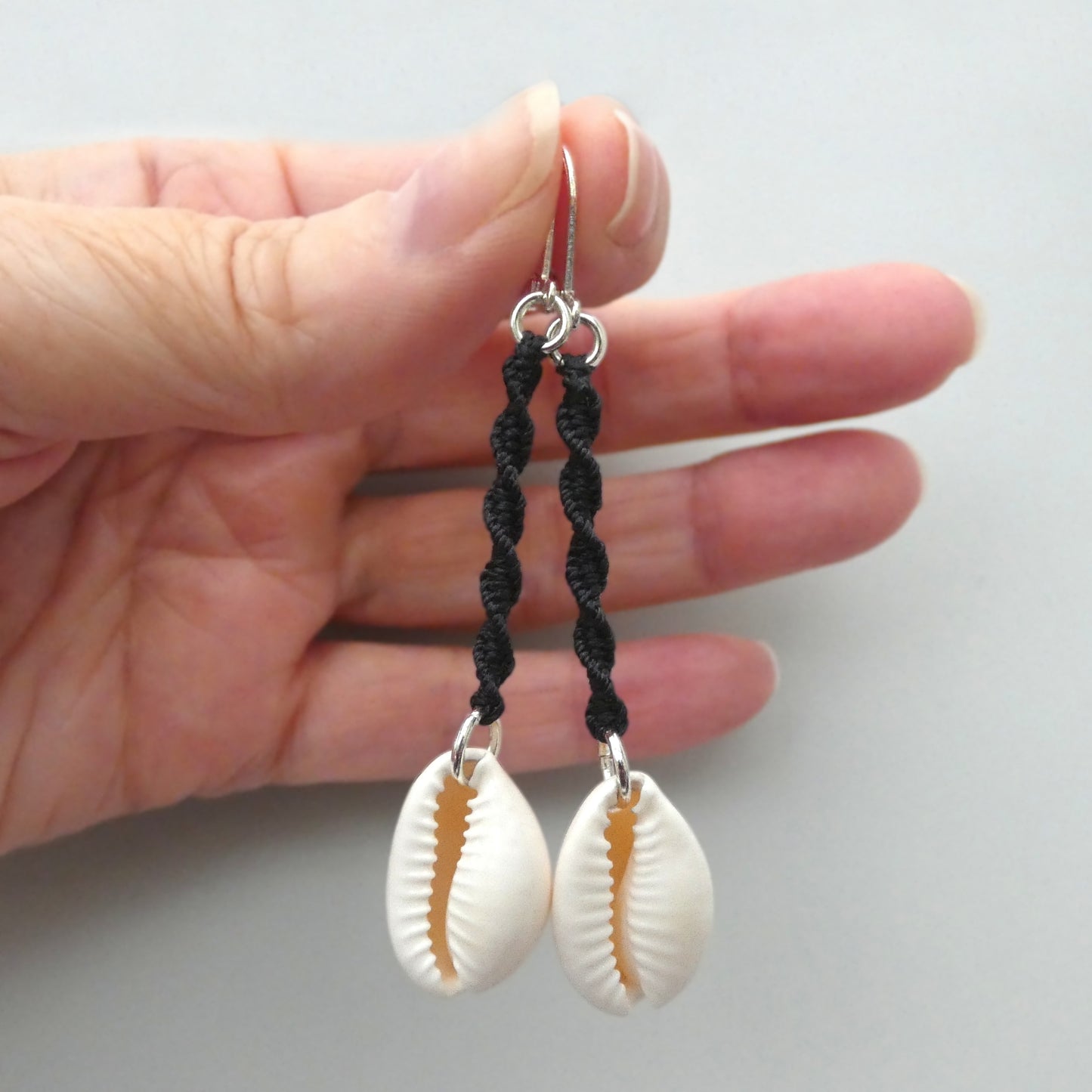 Silver plated leverback earrings with cowrie shells and black macramé twist detail.