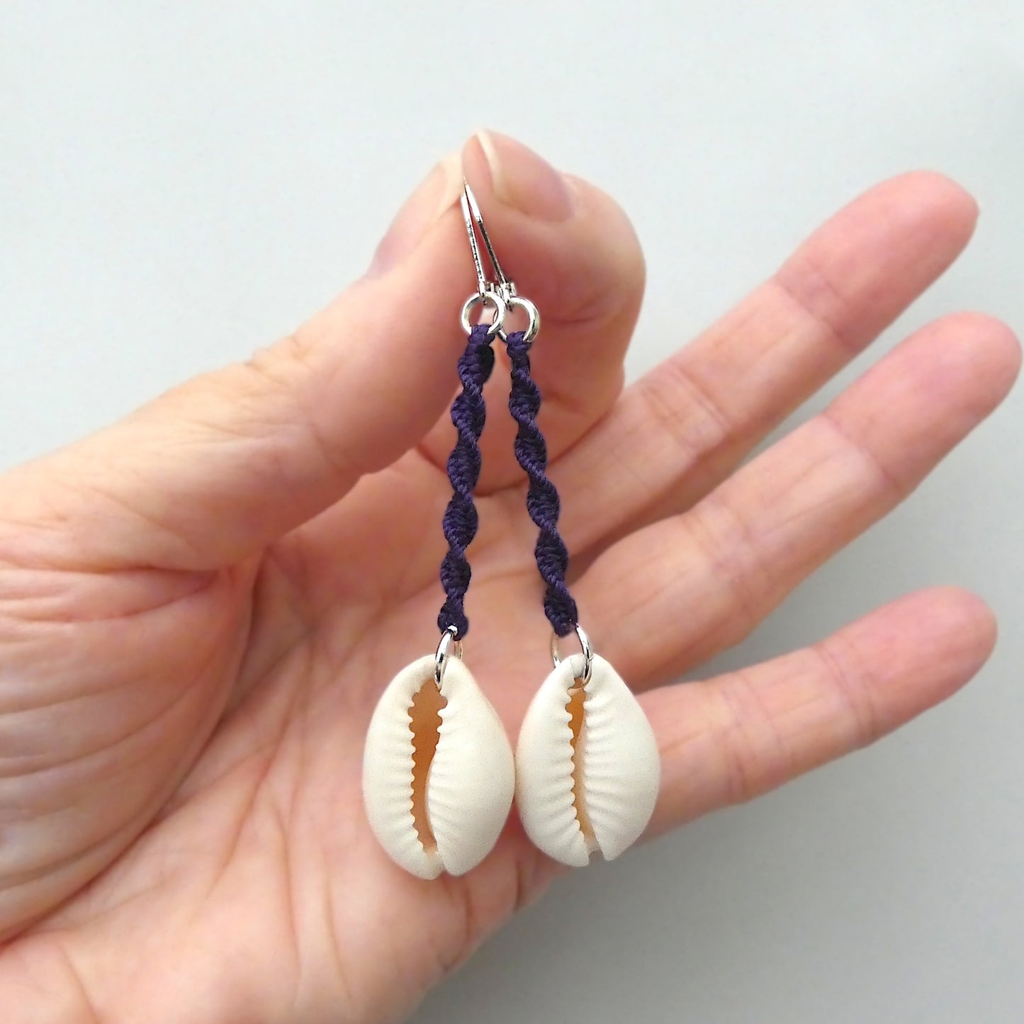 Silver plated leverback earrings with cowrie shells and dark purple macramé twist detail.