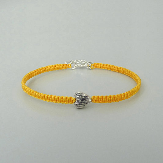 Golden yellow seven inch macramé bracelet with silver plated textured heart charm, lobster clasp and one inch extender chain.