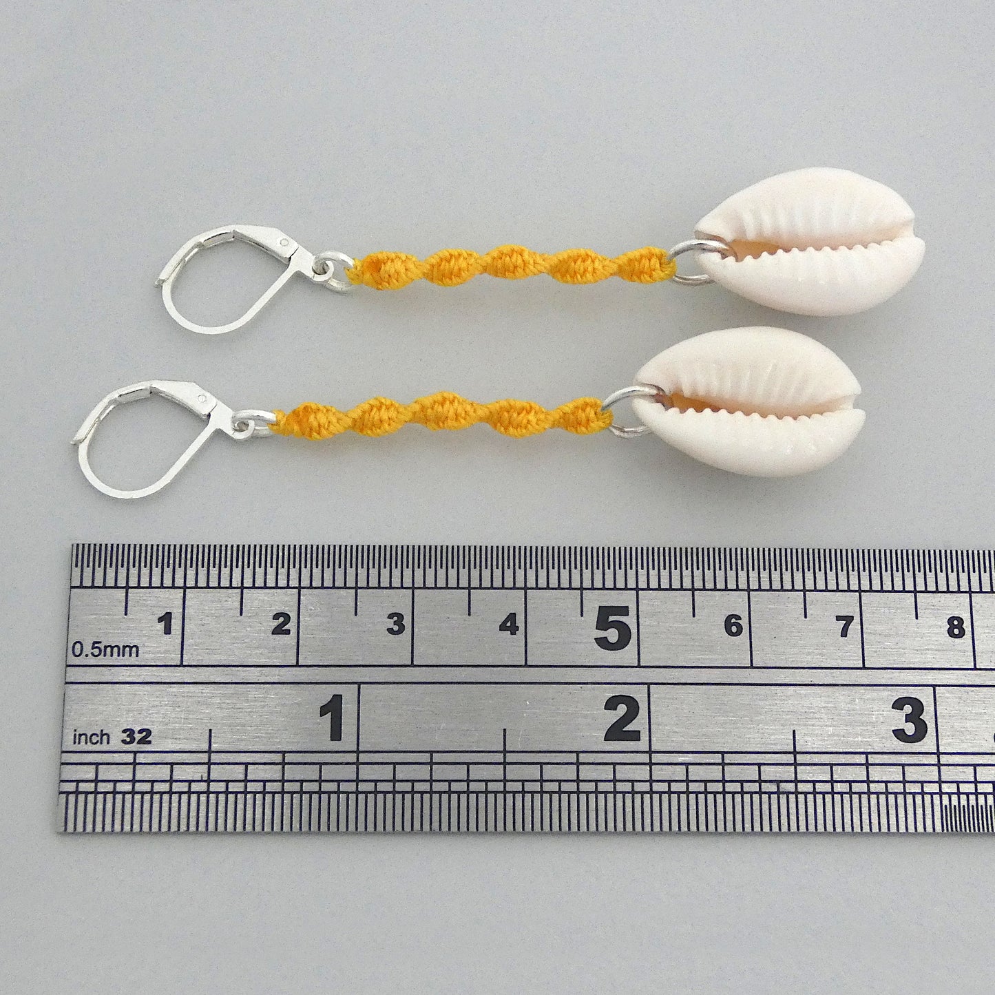 Silver plated leverback earrings with cowrie shells and golden yellow macramé twist detail.