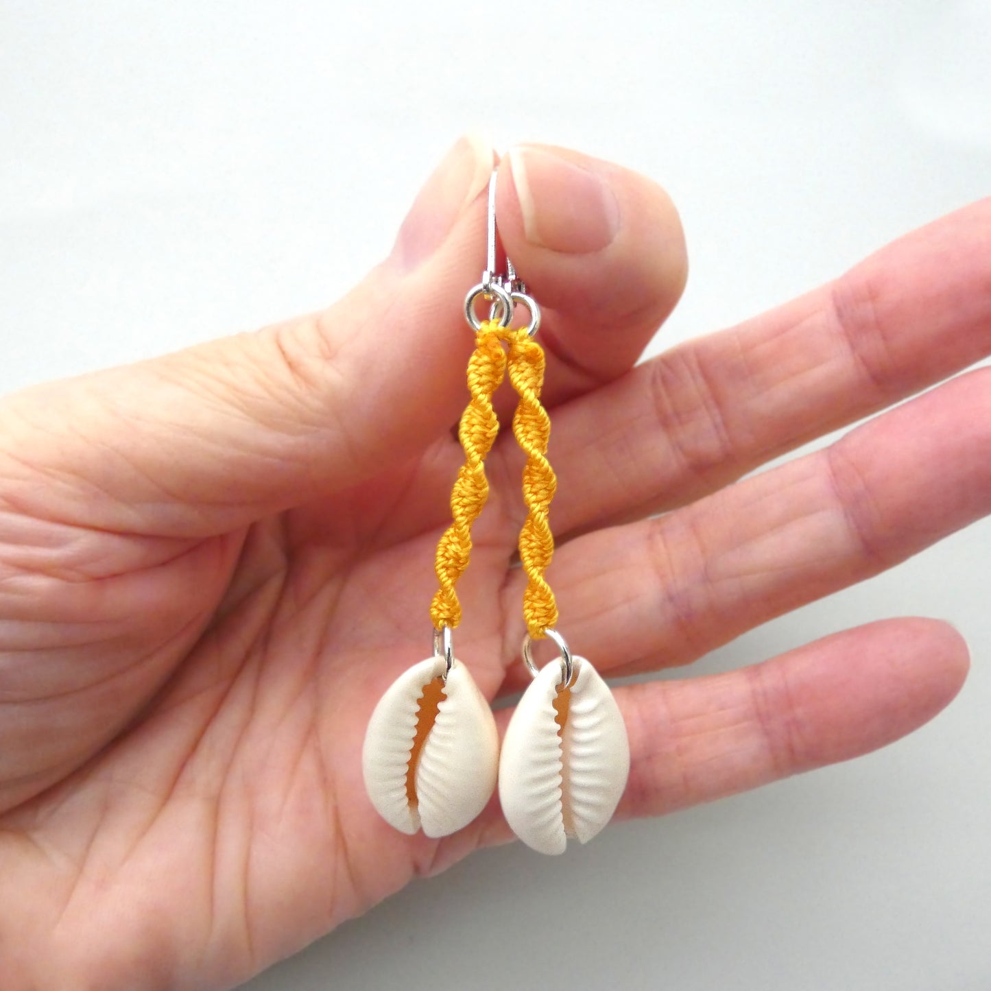 Silver plated leverback earrings with cowrie shells and golden yellow macramé twist detail.