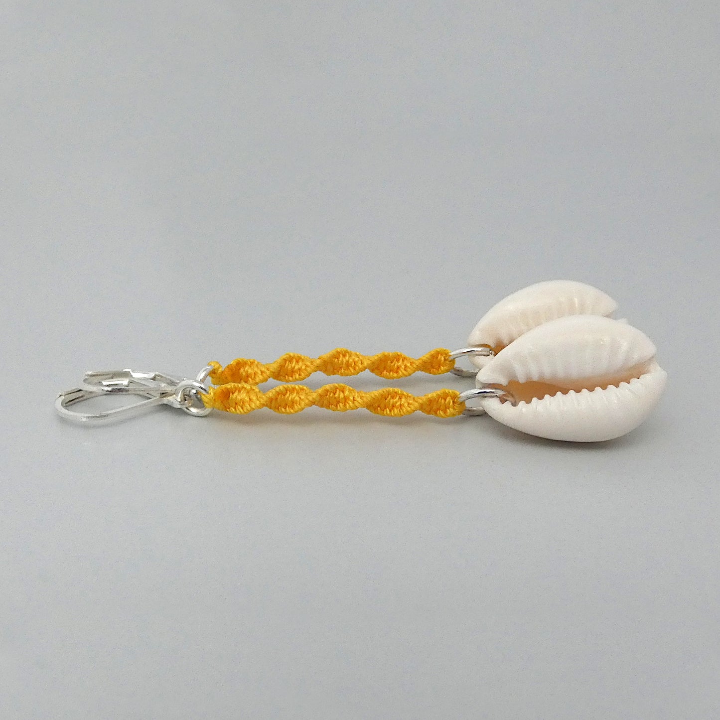 Silver plated leverback earrings with cowrie shells and golden yellow macramé twist detail.