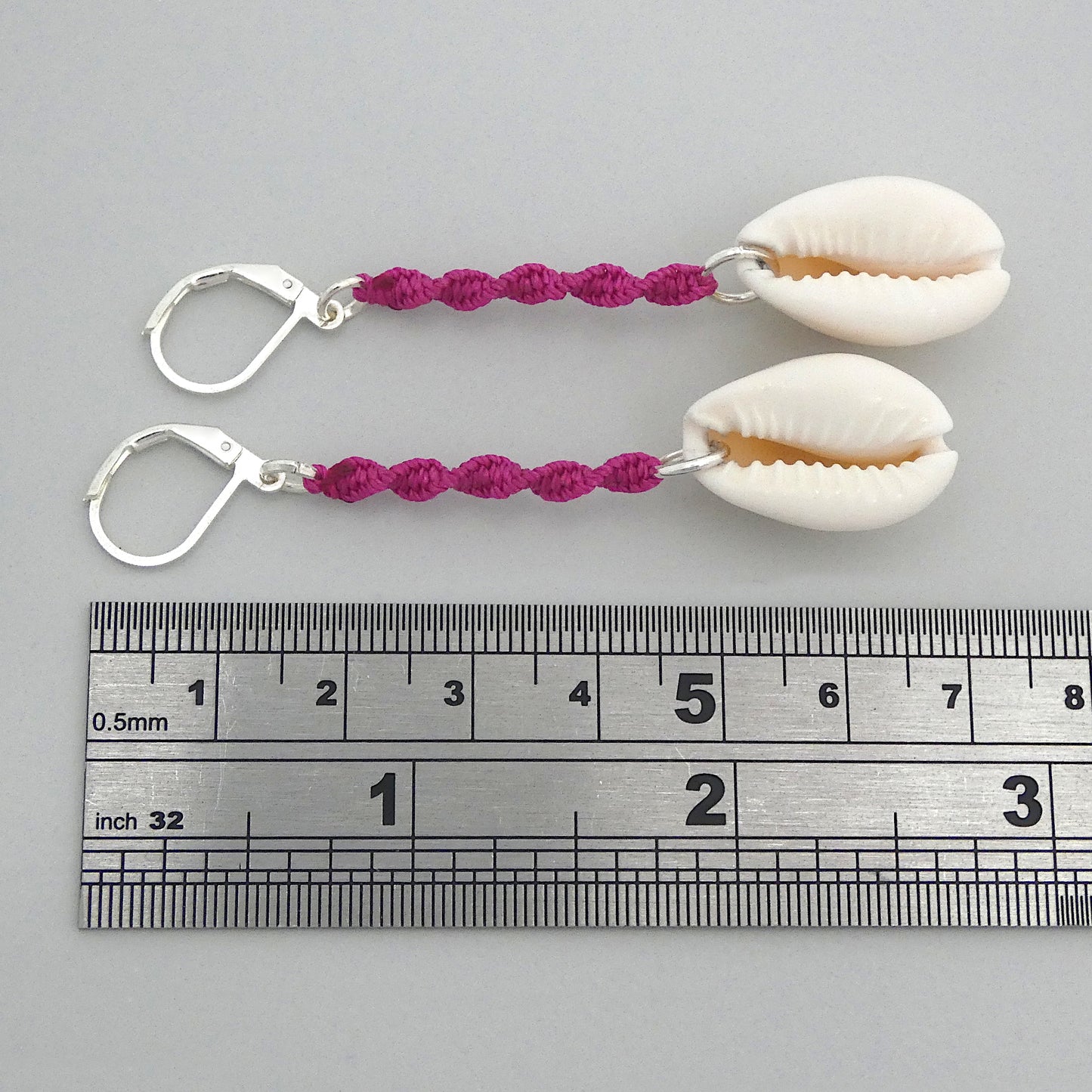 Silver plated leverback earrings with cowrie shells and magenta macramé twist detail.