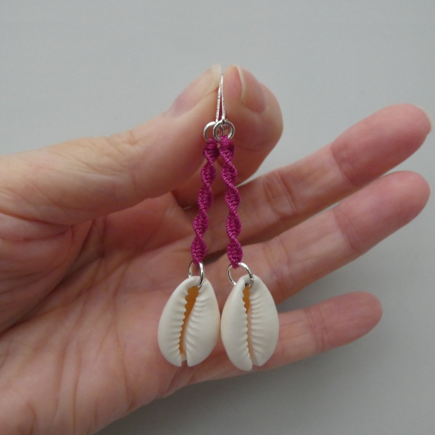 Silver plated leverback earrings with cowrie shells and magenta macramé twist detail.