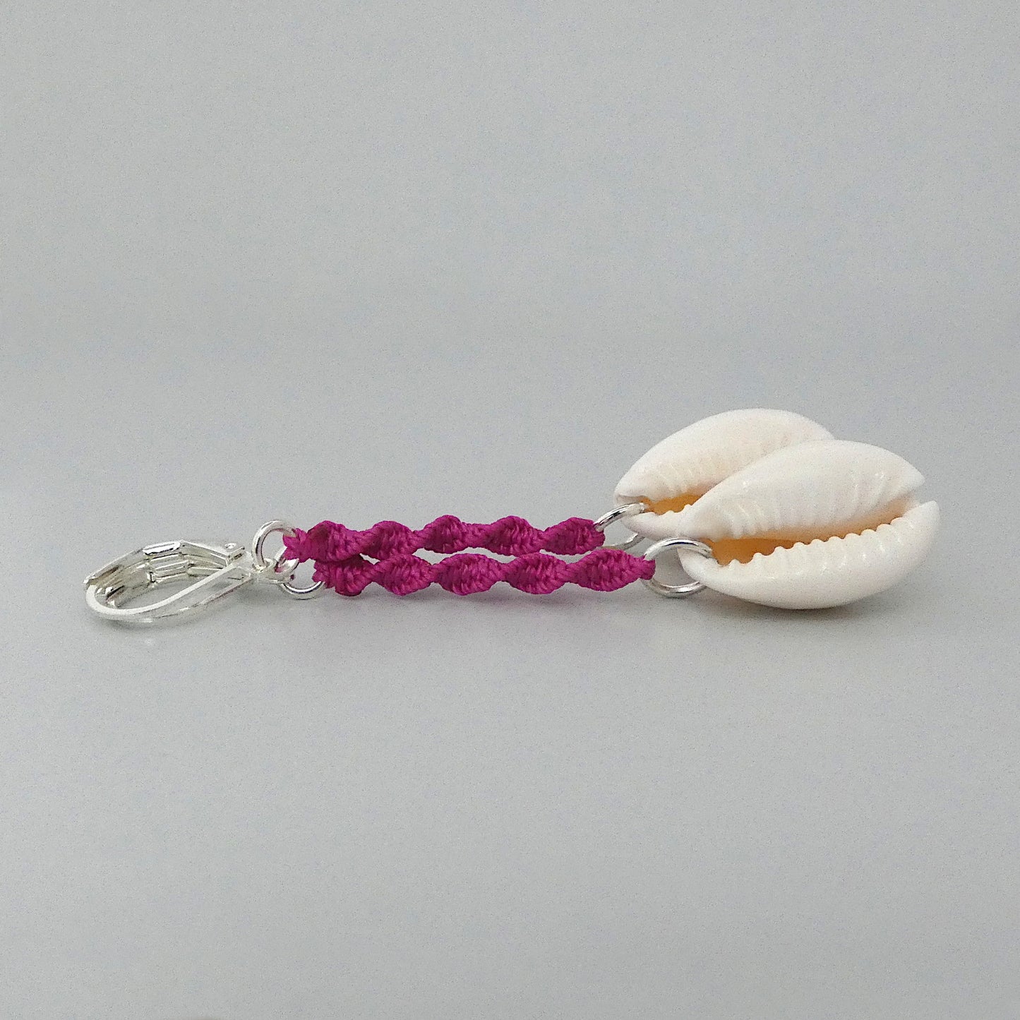 Silver plated leverback earrings with cowrie shells and magenta macramé twist detail.