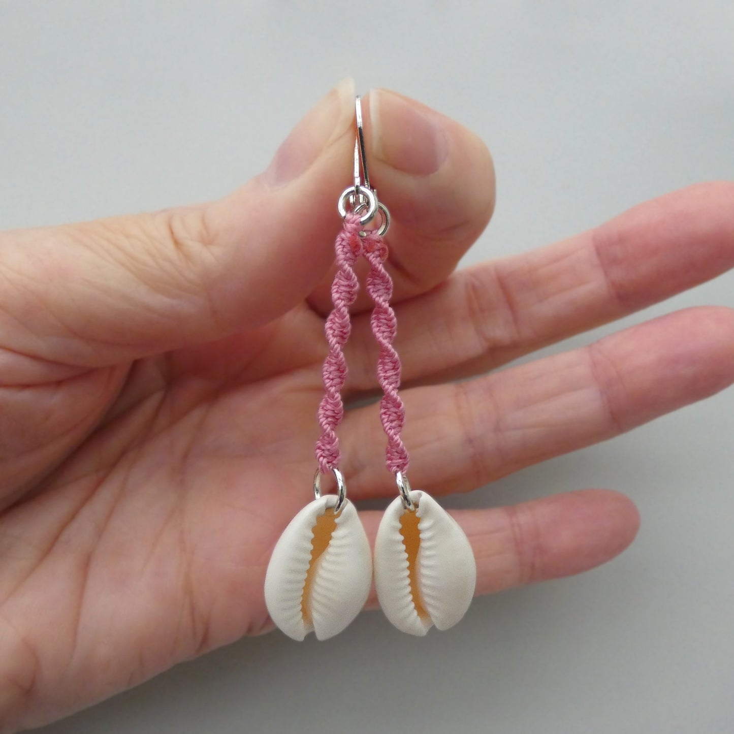 Silver plated leverback earrings with cowrie shells and pink macramé twist detail.