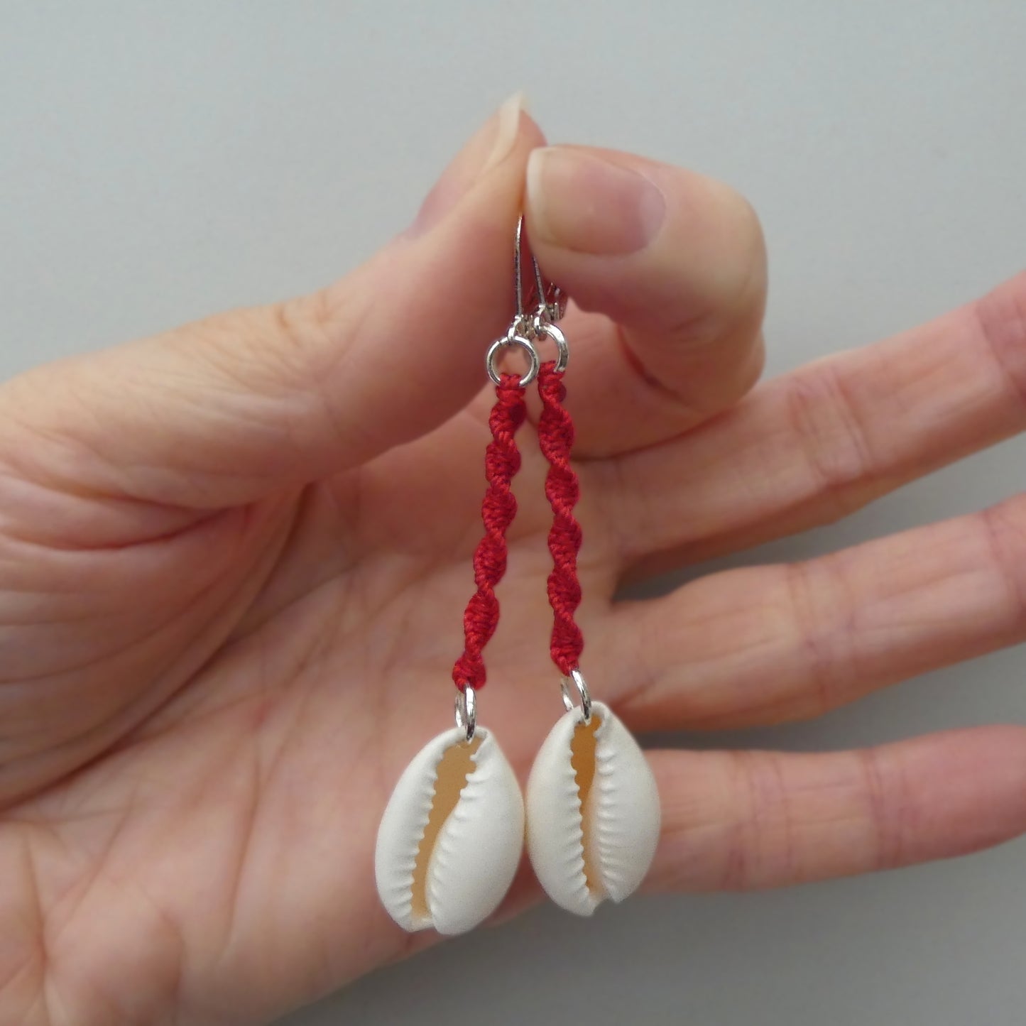 Silver plated leverback earrings with cowrie shells and bright red macramé twist detail.