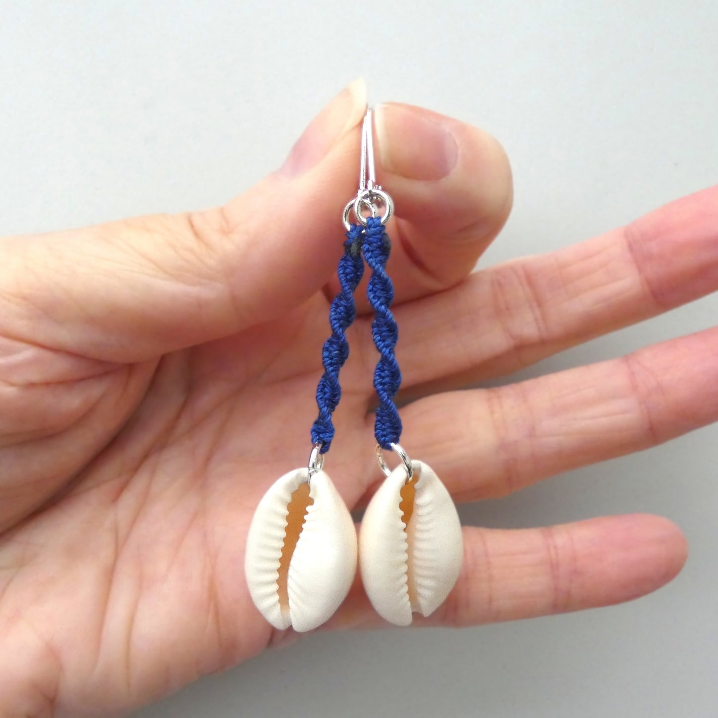 Silver plated leverback earrings with cowrie shells and royal blue macramé twist detail.