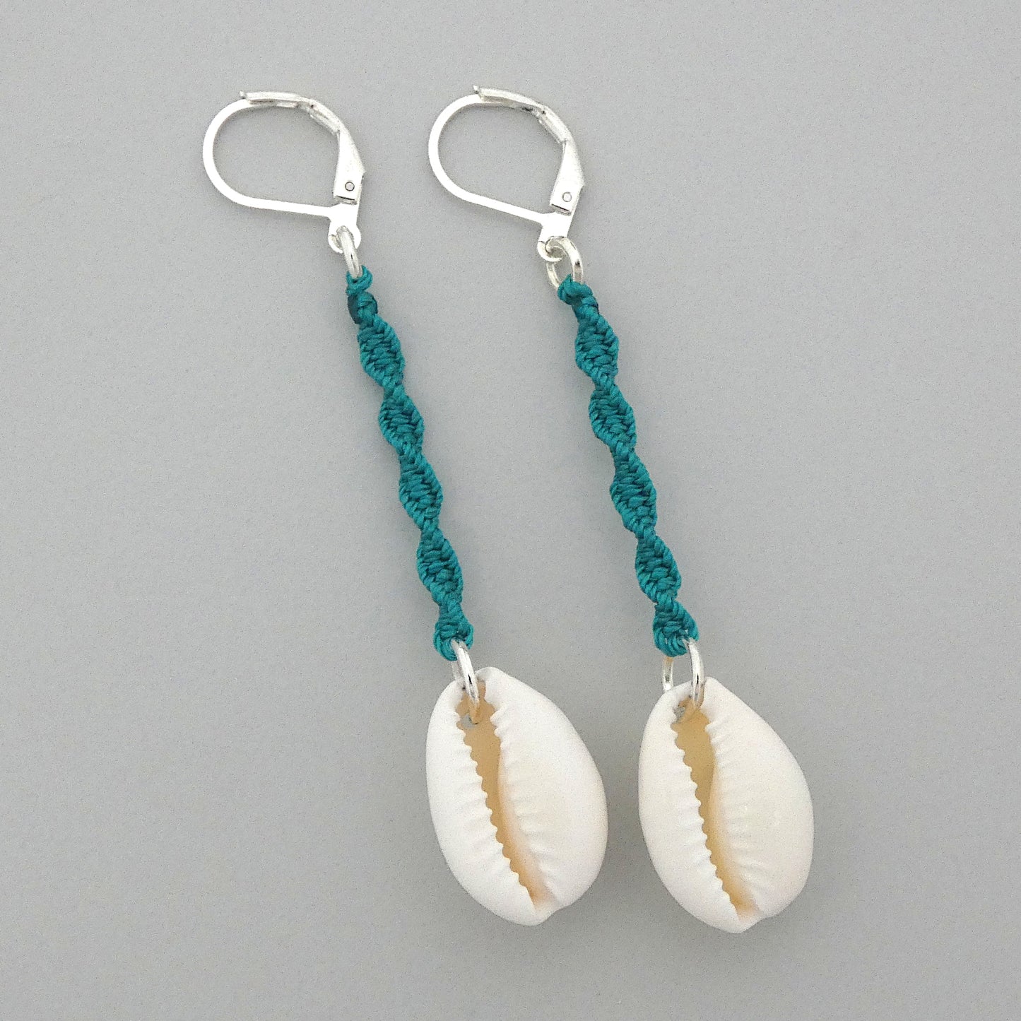 Silver plated leverback earrings with cowrie shells and teal green macramé twist detail.