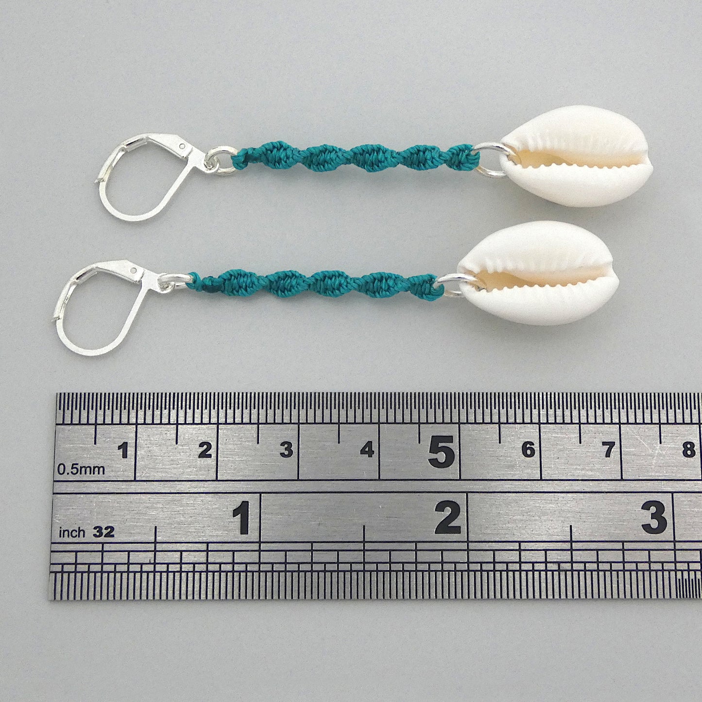 Silver plated leverback earrings with cowrie shells and teal green macramé twist detail.