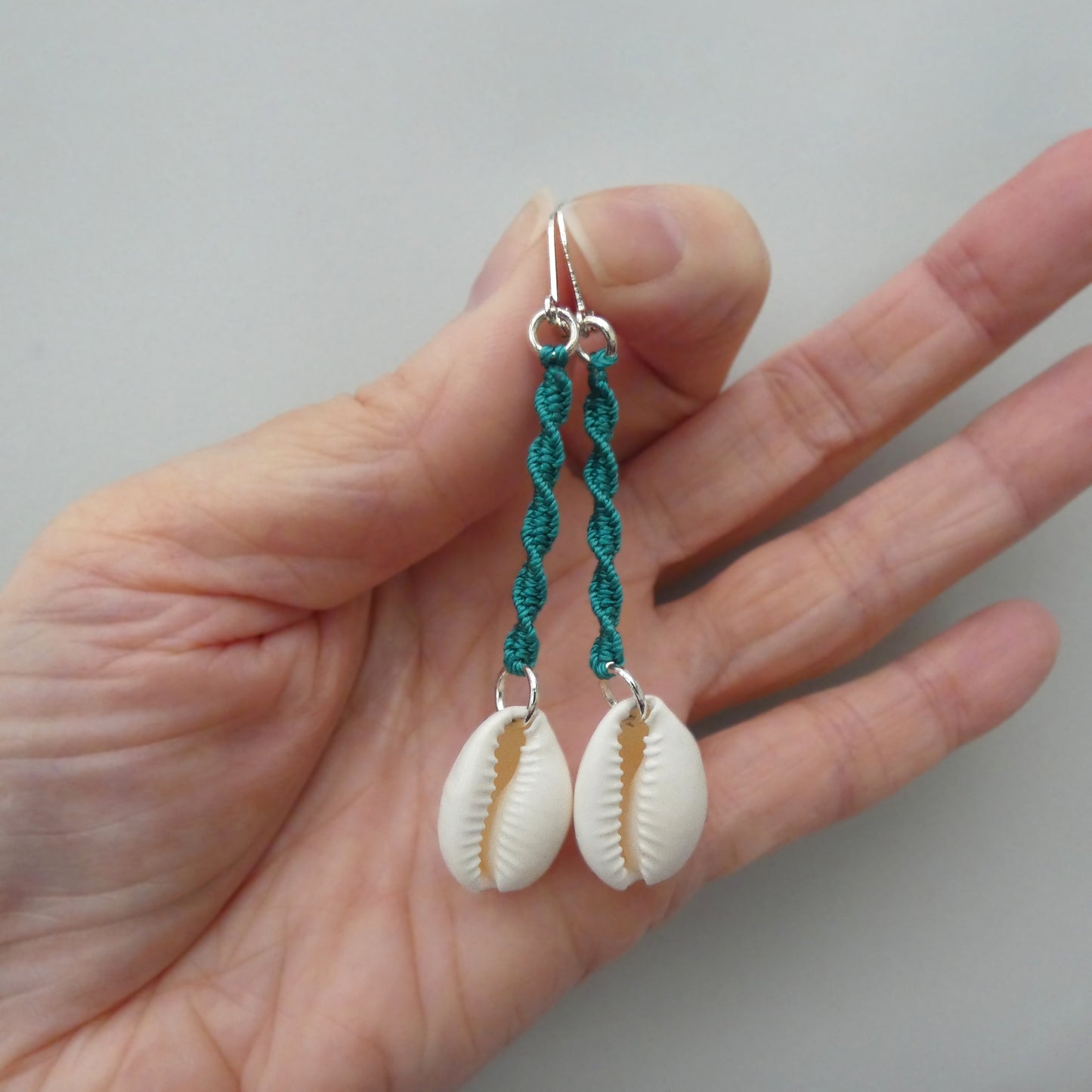 Silver plated leverback earrings with cowrie shells and teal green macramé twist detail.