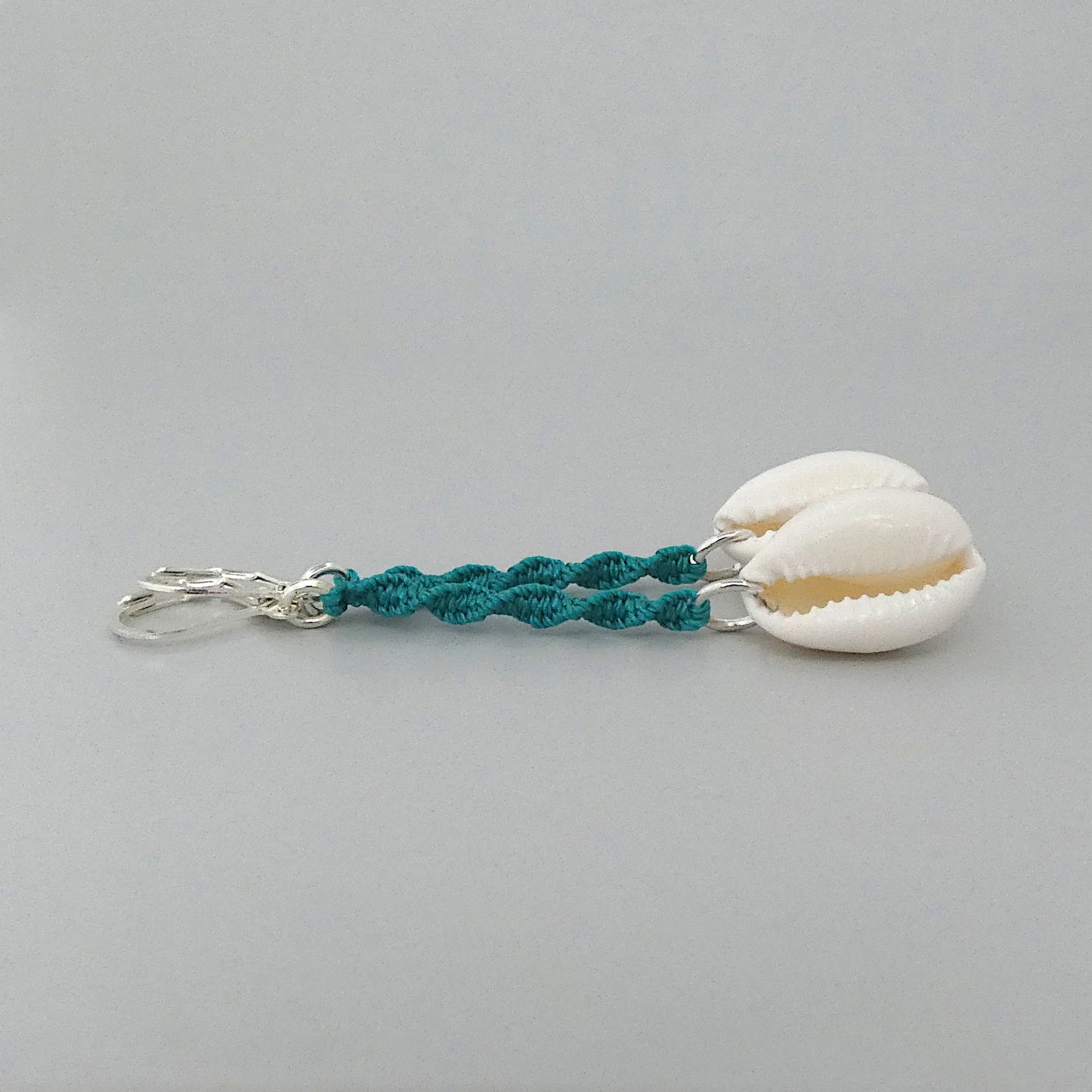 Silver plated leverback earrings with cowrie shells and teal green macramé twist detail.