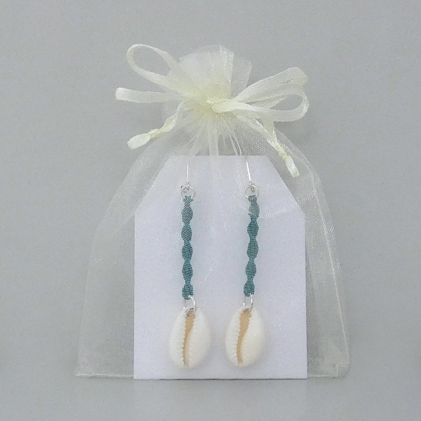 Silver plated leverback earrings with cowrie shells and teal green macramé twist detail.