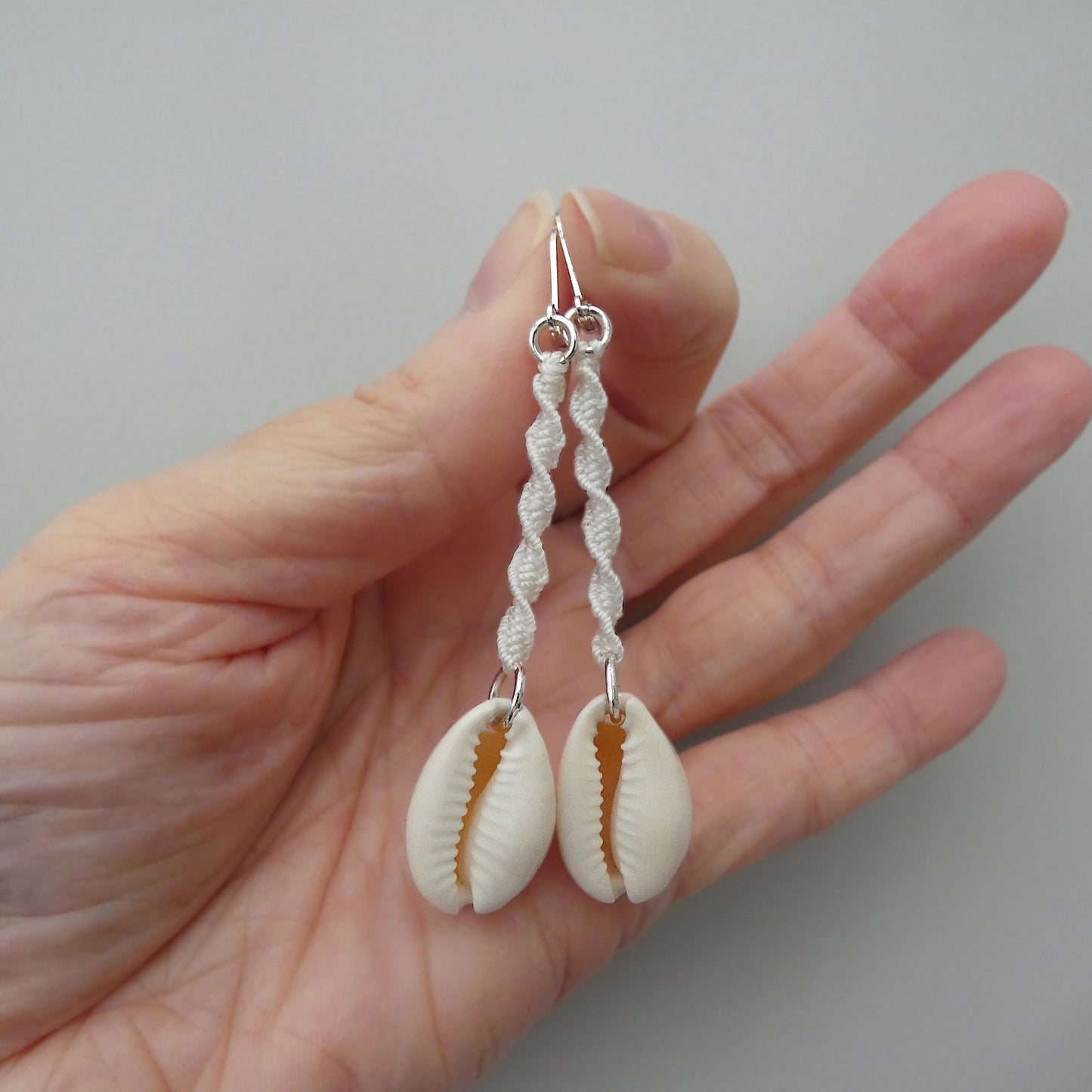 Silver plated leverback earrings with cowrie shells and white macramé twist detail.